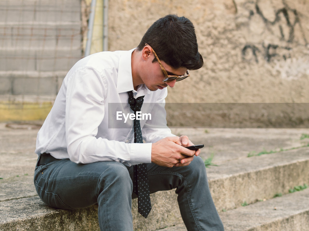 Man wearing tie using phone while sitting on steps