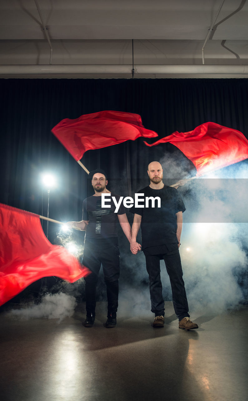 Full length portrait of men with red flags standing against smoke at night