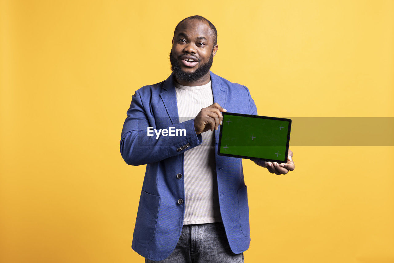 portrait of young man using digital tablet while standing against blue background