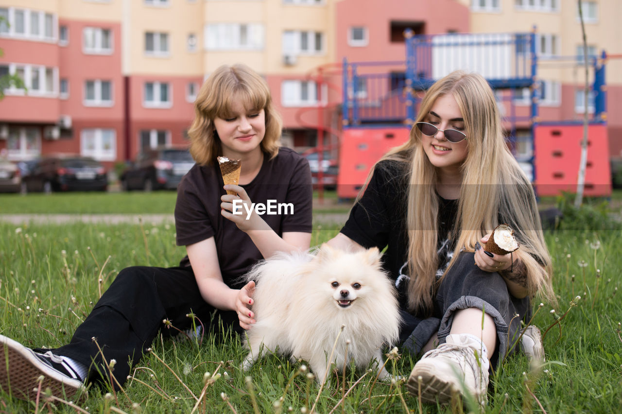 Two funny girls are eating ice cream and playing with a pomeranian dog. holidays