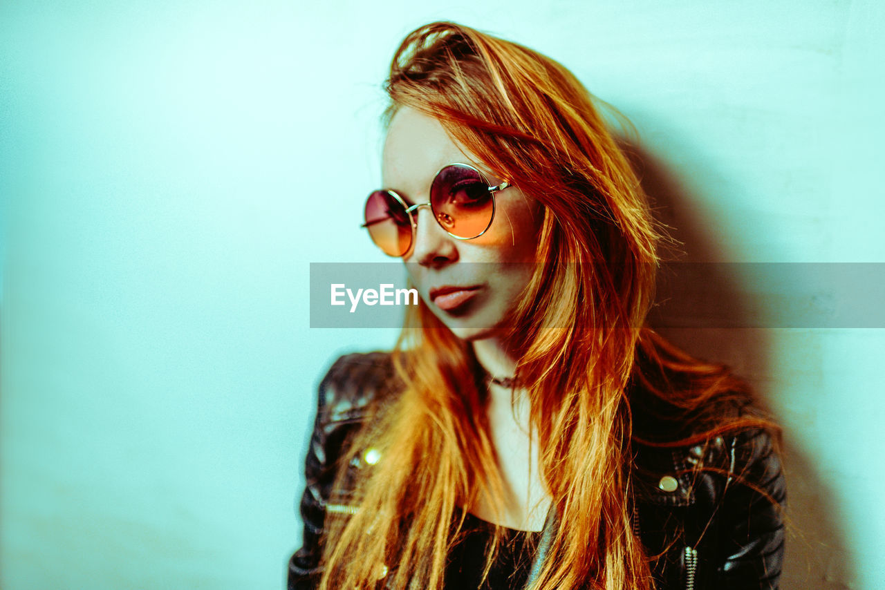 portrait of young woman wearing sunglasses against white wall