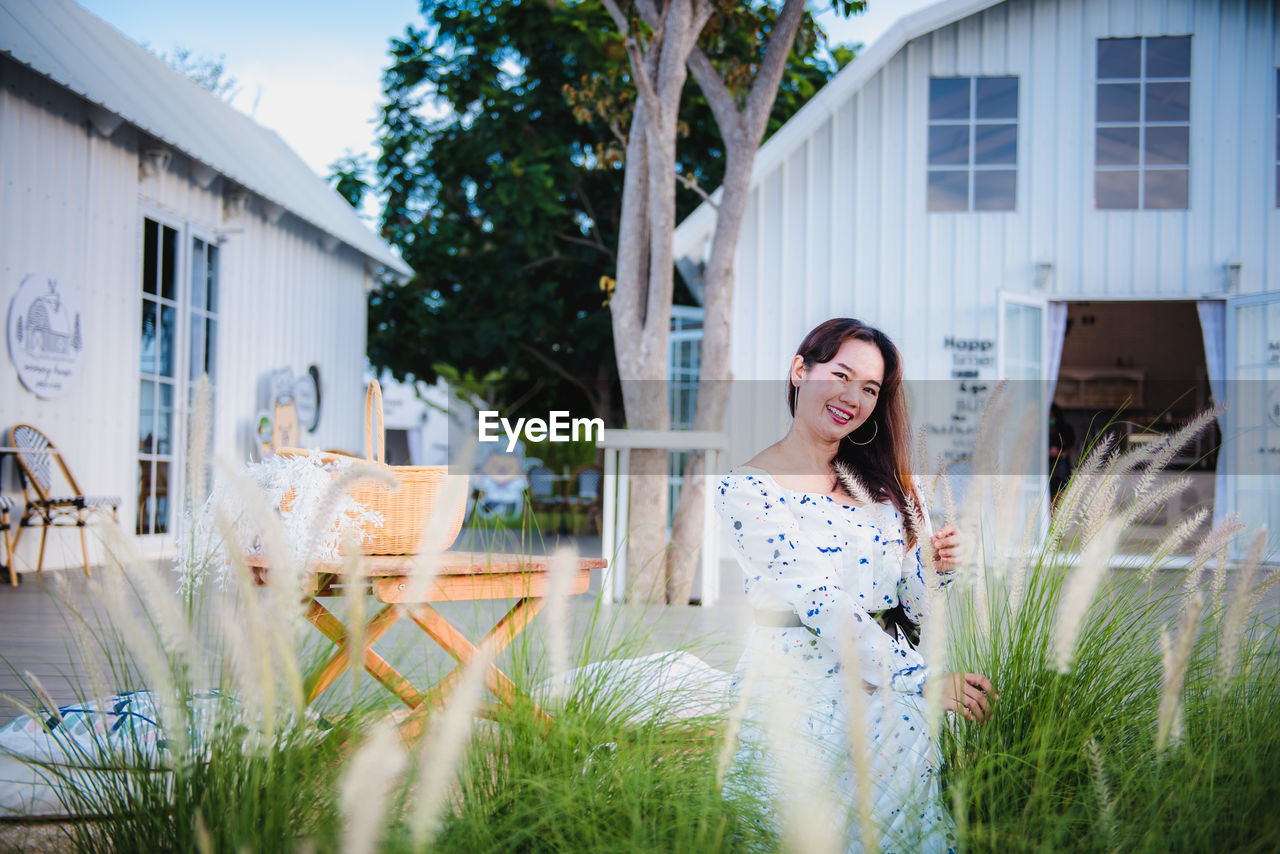 PORTRAIT OF SMILING WOMAN STANDING AGAINST PLANTS