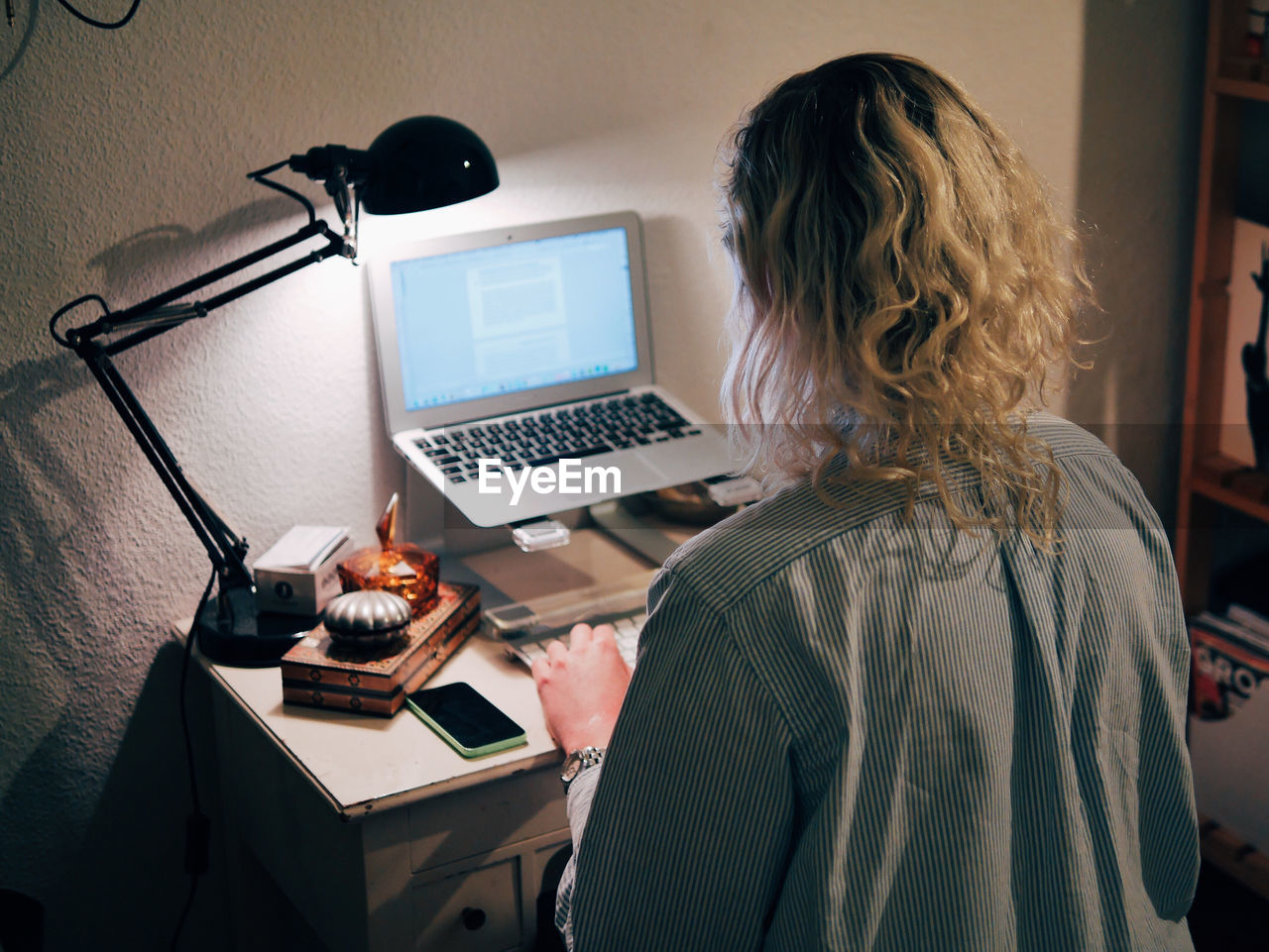 Rear view of woman using laptop while sitting at home