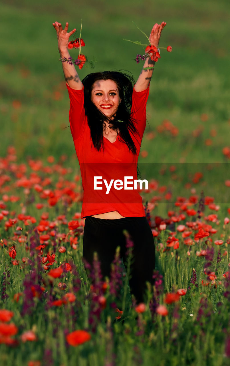 PORTRAIT OF SMILING YOUNG WOMAN STANDING BY RED FLOWER