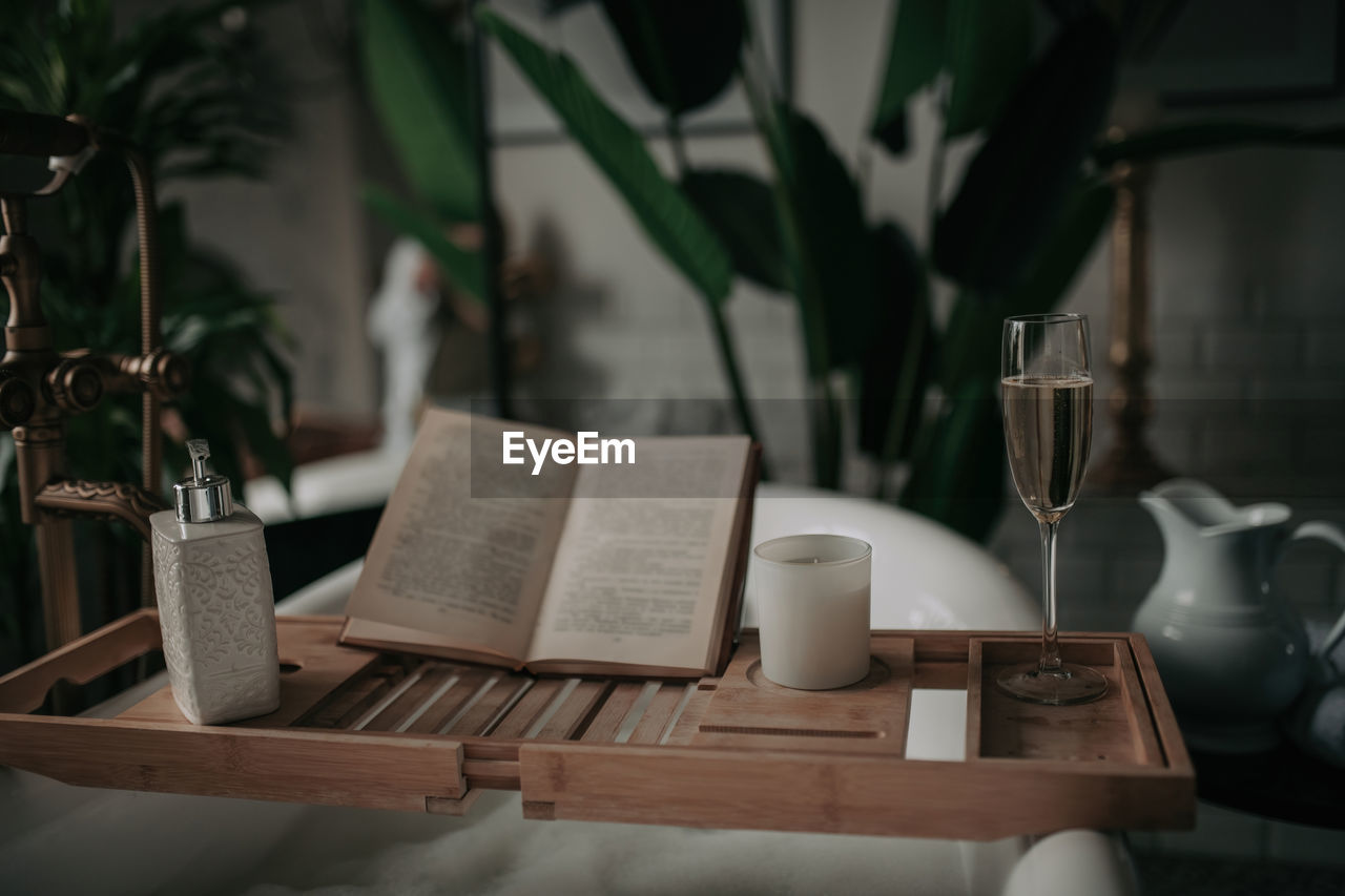 table, drink, food and drink, book, publication, cup, indoors, mug, tableware, no people, coffee cup, refreshment, plant, paper, furniture, household equipment, coffee, nature, wood, focus on foreground, vase, glass, restaurant, room, seat, business