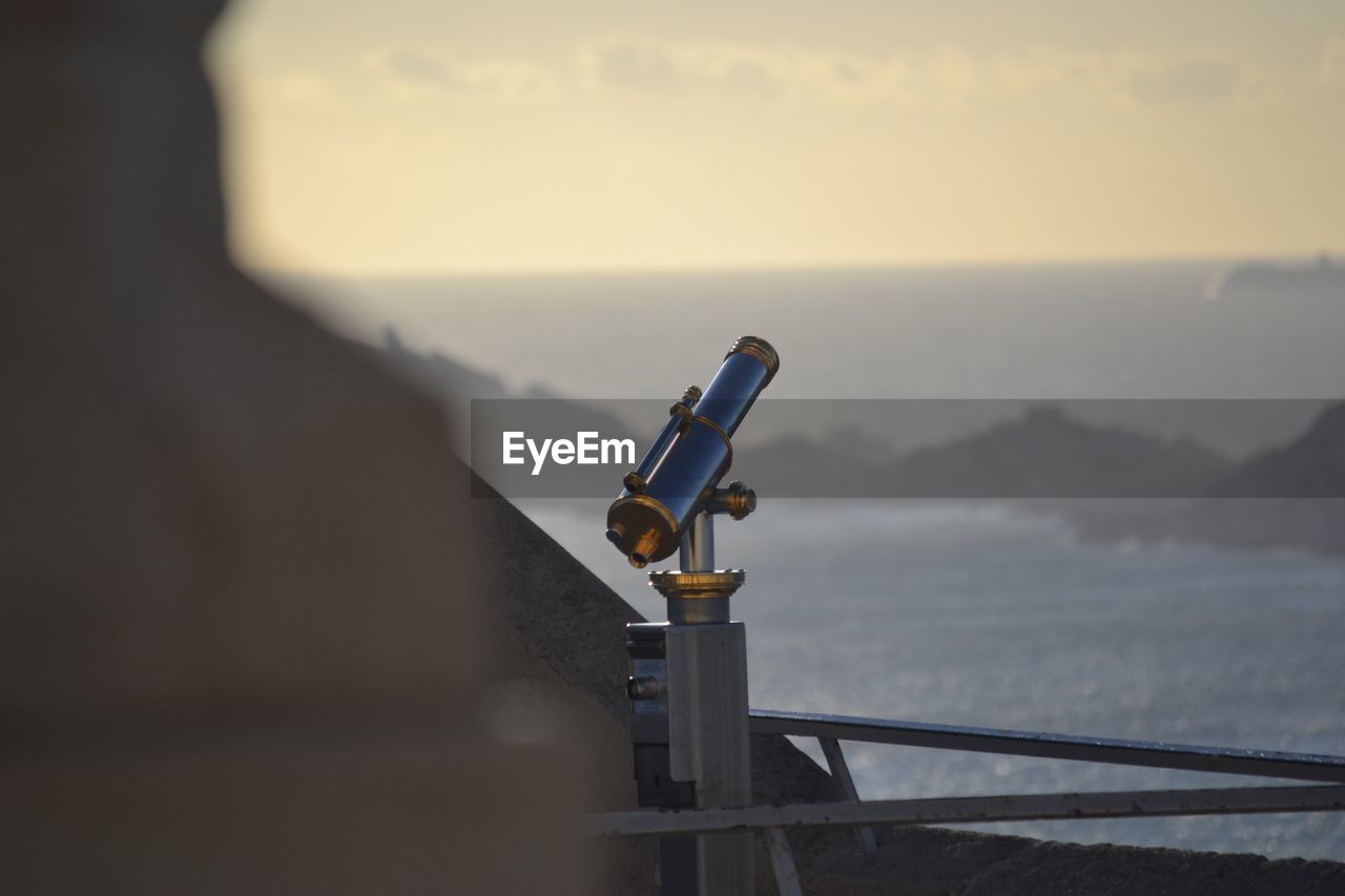 CLOSE-UP OF COIN-OPERATED BINOCULARS ON SEA AGAINST SKY