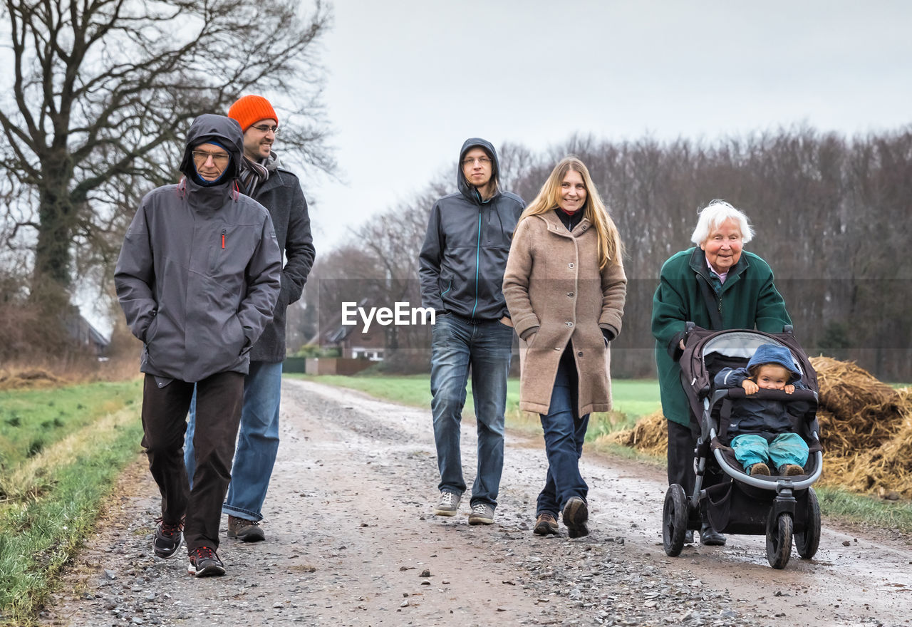 Multi-generation family in warm clothing walking on dirt road against sky