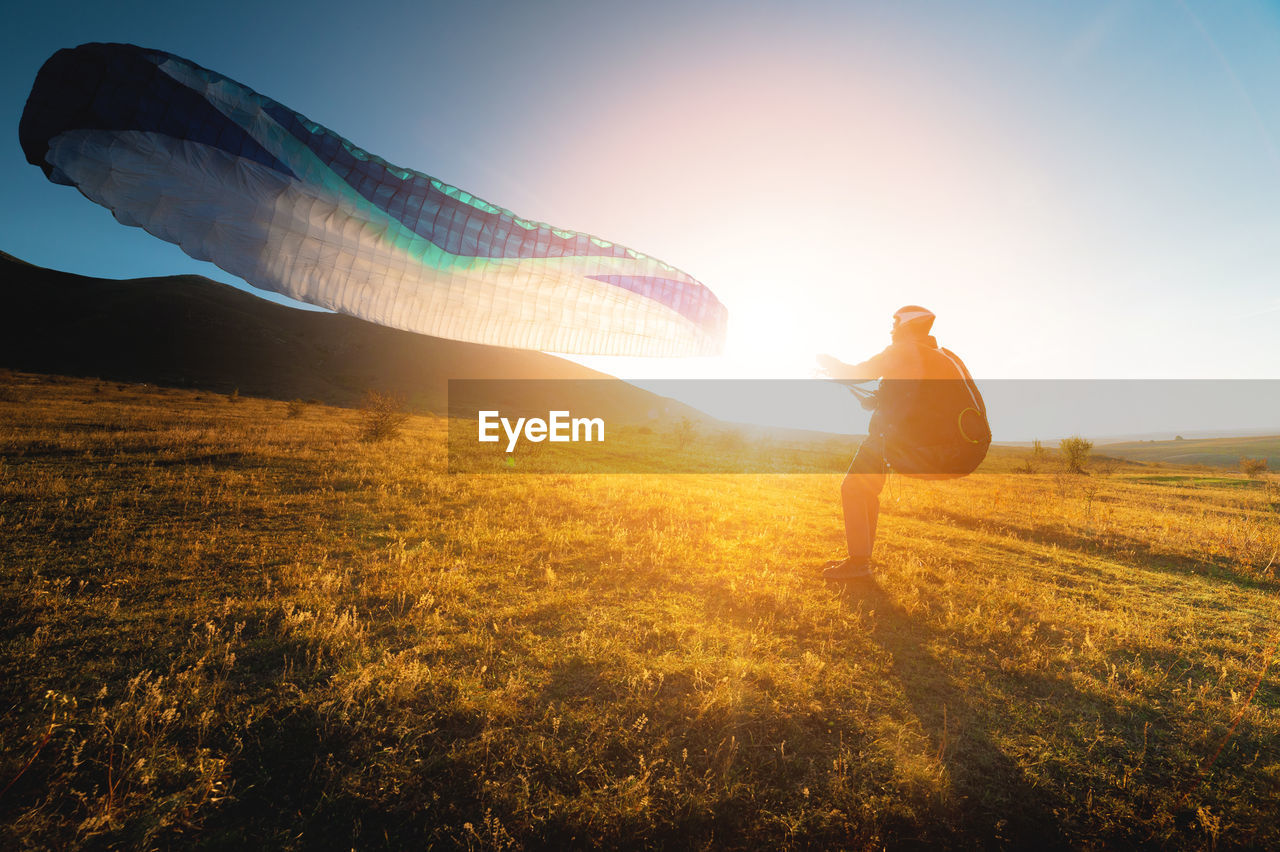 Paraglider with a blue parachute takes off. a male athlete stands on the field and lifts a