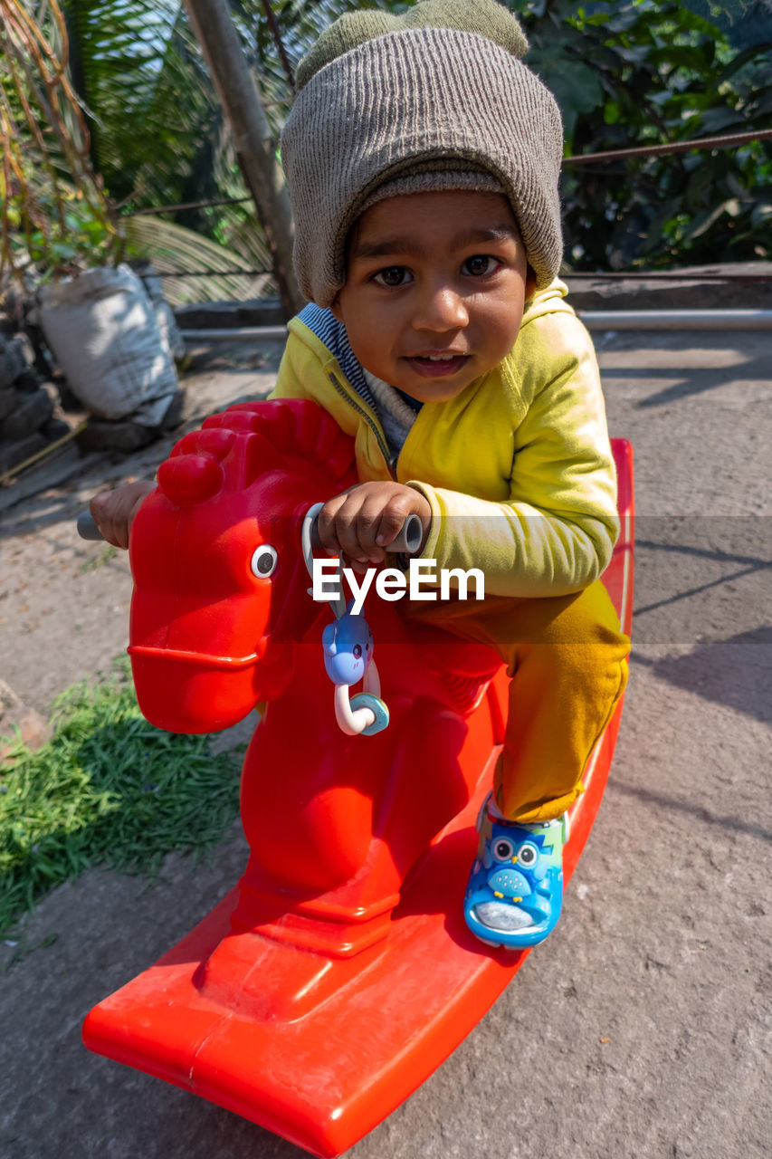 PORTRAIT OF CUTE BOY HOLDING TOY WHILE SITTING ON FLOOR