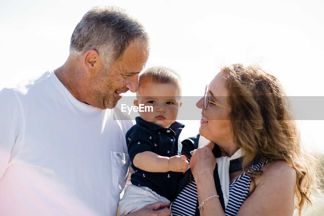 Grandparents smiling & holding grandson on beach