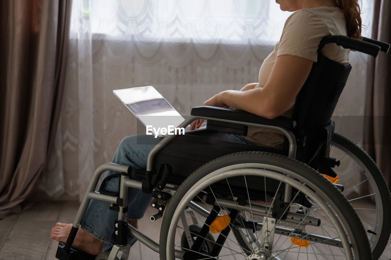 Midsection of woman using laptop sitting on wheelchair