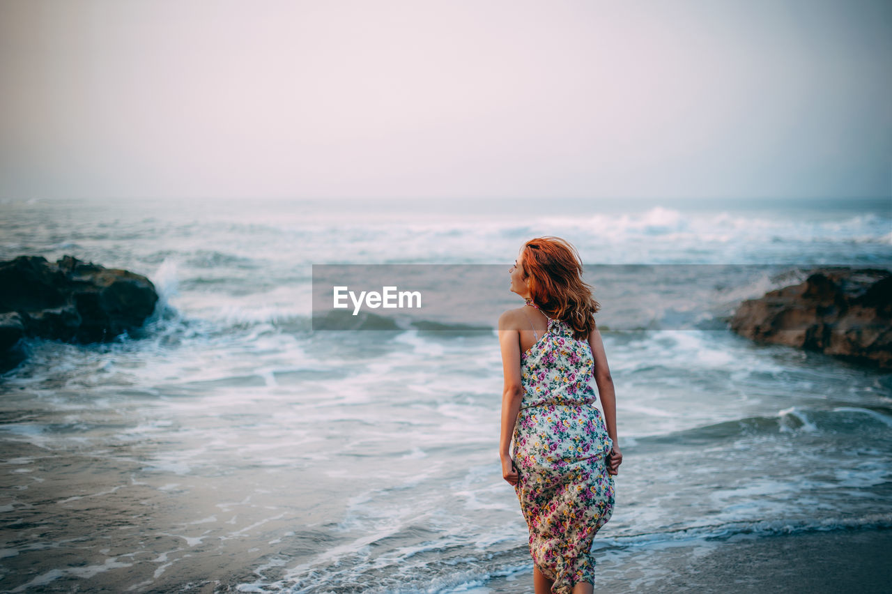 Rear view of woman standing on shore against sky