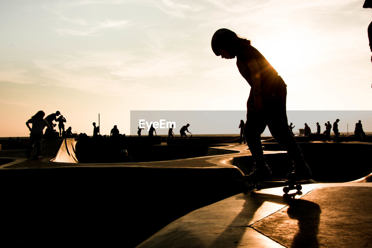 Silhouette woman skateboarding against sky at park during sunset