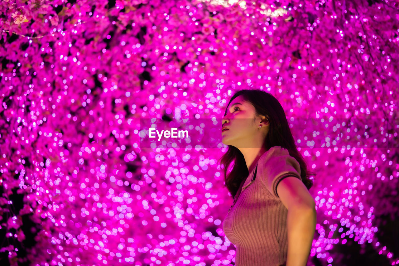 Low angle view of woman standing against illuminated tree at night