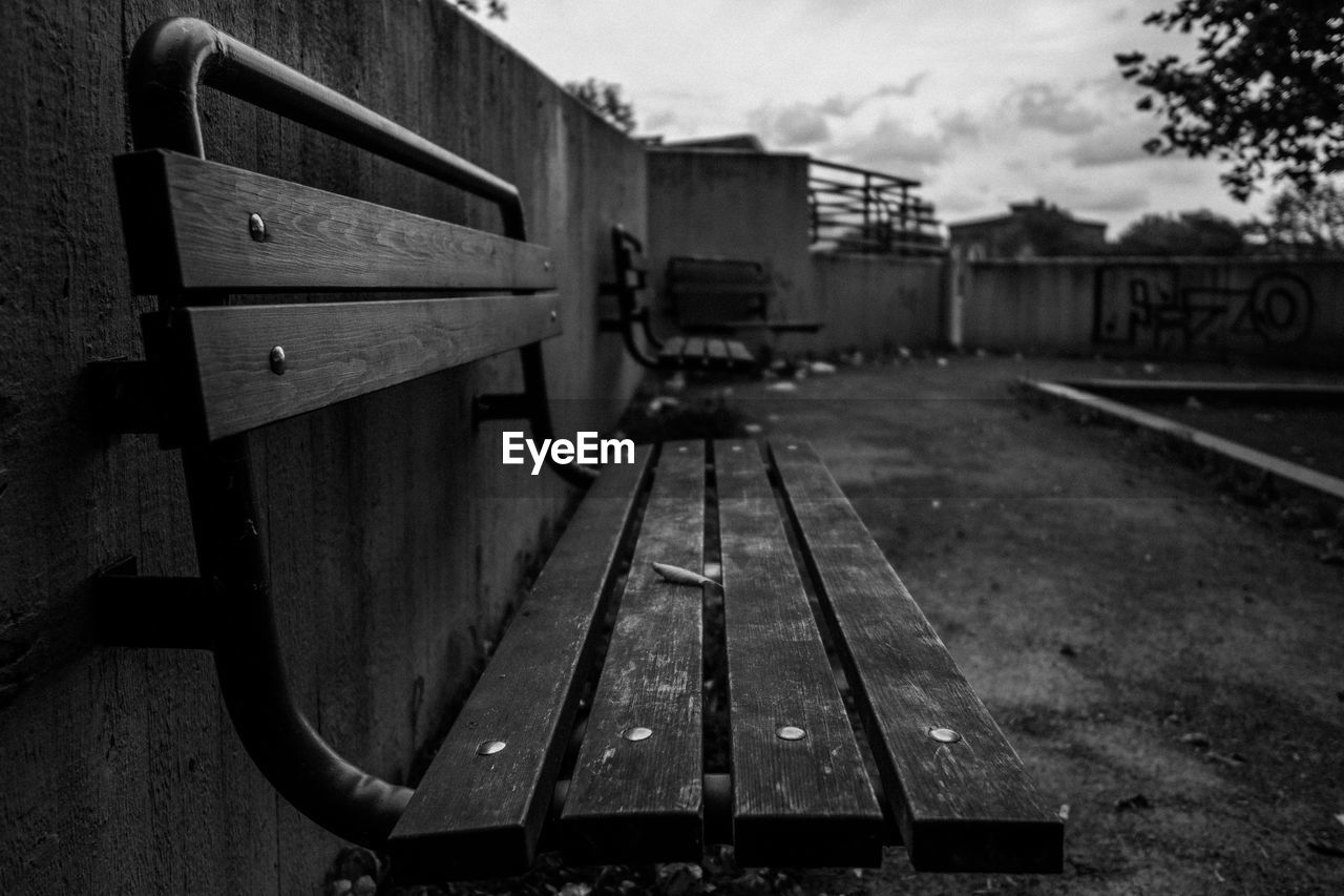 Close-up of empty bench by fence against sky