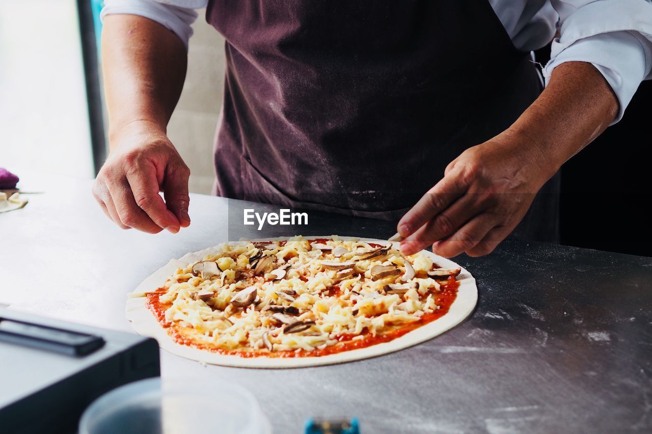 Midsection of man preparing pizza food in kitchen sprinkling some salt