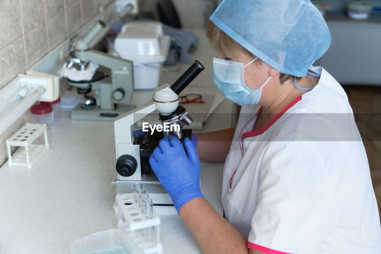 Woman scientist wearing face mask and protective gloves working in laboratory looking 