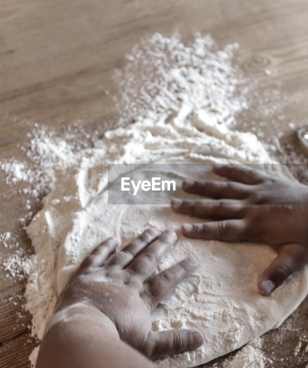 Cropped hands on kid flattening dough on table
