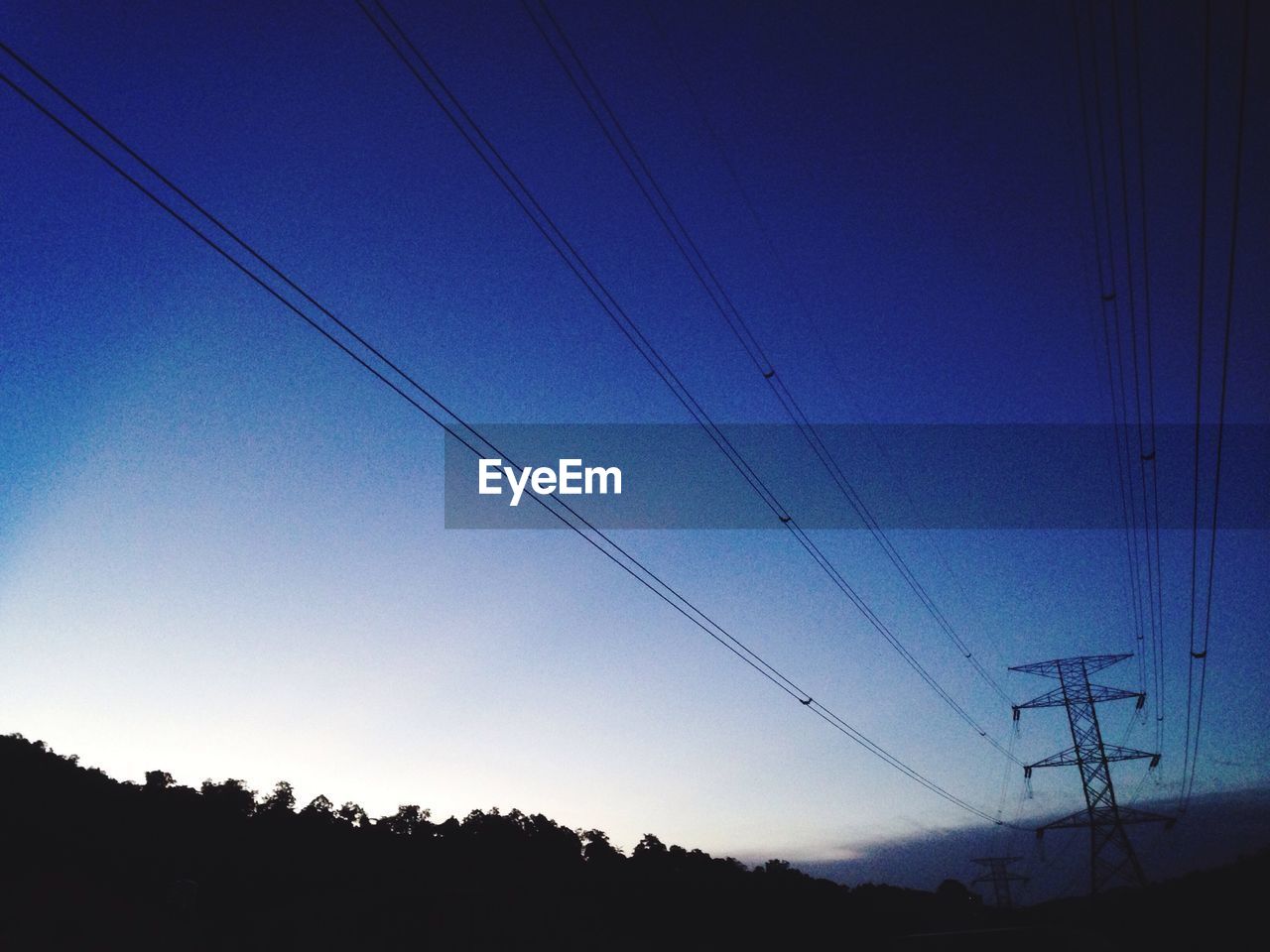 LOW ANGLE VIEW OF SILHOUETTE ELECTRICITY PYLON AGAINST BLUE SKY