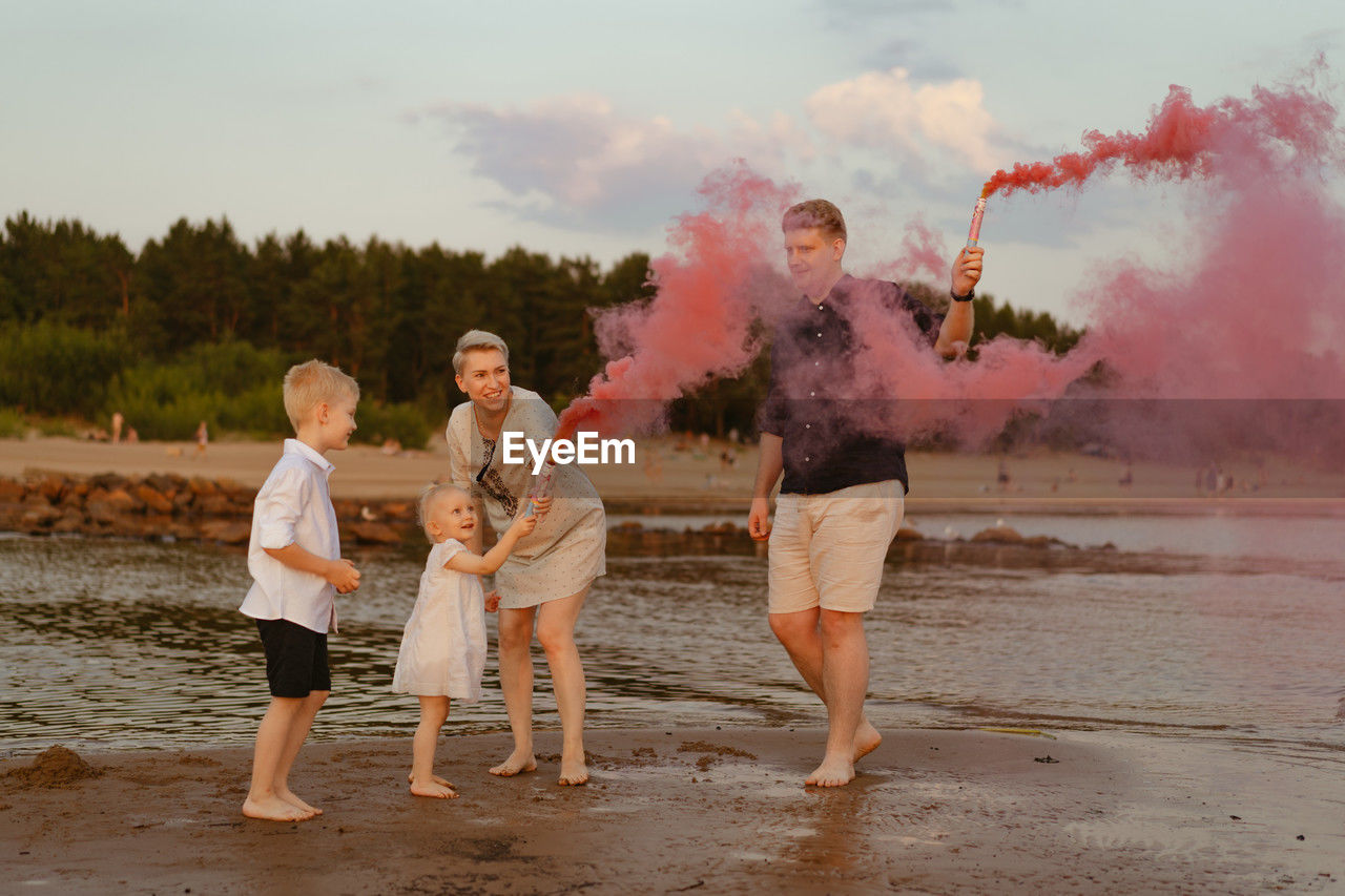 rear view of family standing at beach during sunset