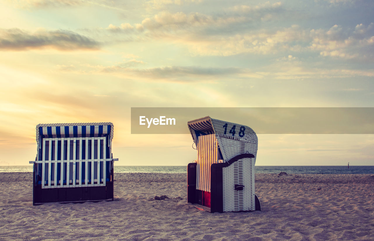 Hooded beach chairs against sky during sunset