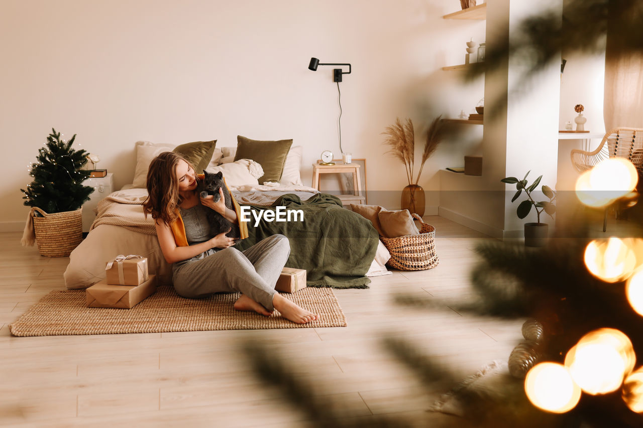 A pretty girl in pajamas rejoices and smiles during the christmas holidays in cozy bedroom interior