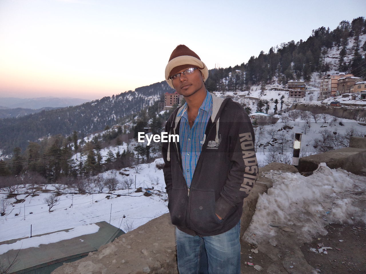 Portrait of man standing by snow covered mountain against sky during sunset