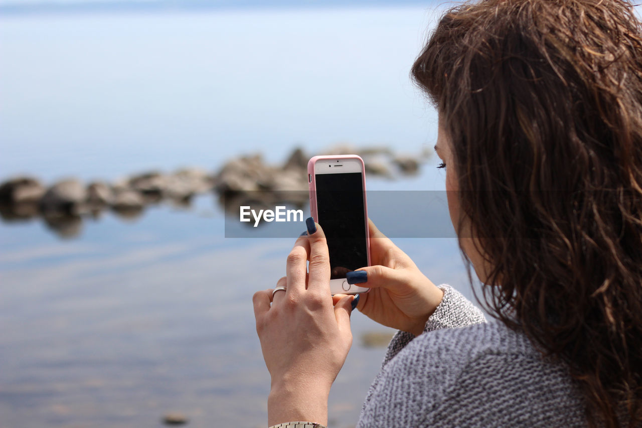 Rear view of woman photographing with mobile phone at beach