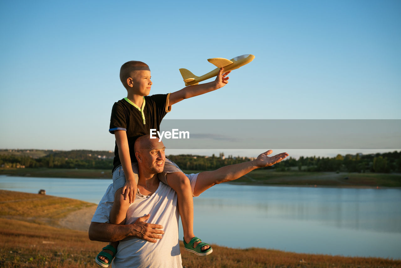 Father holding son on shoulders at sunset with airplane in hand