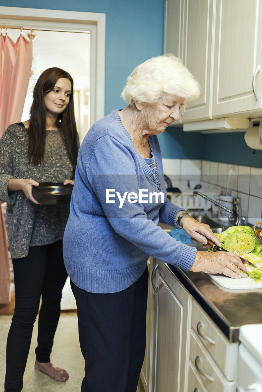 Young woman looking at grandmother preparing food in kitchen