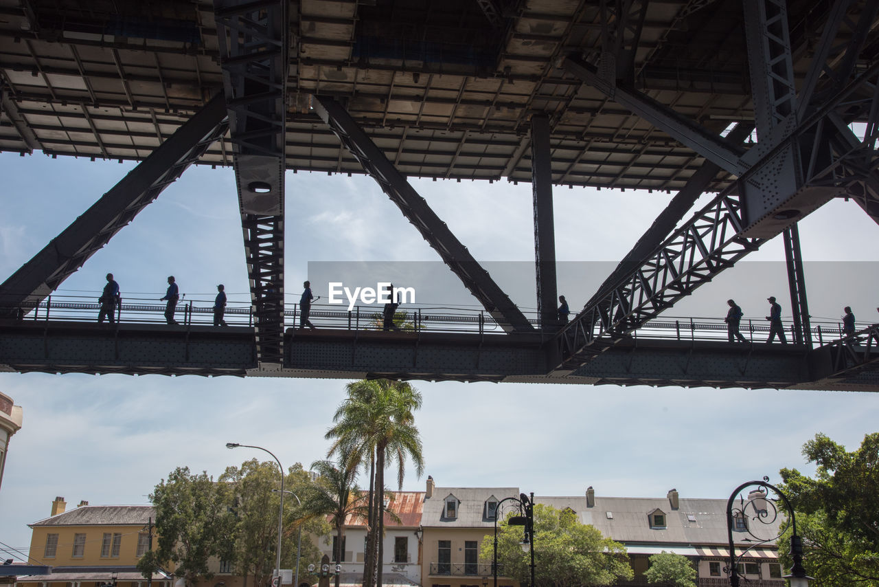 Low angle view of people walking on bridge in city