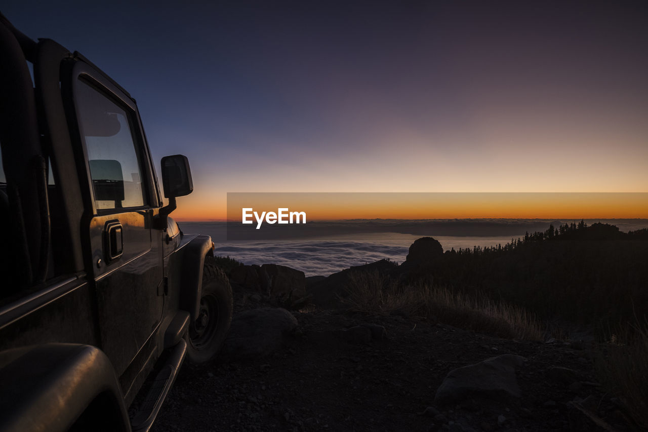 Vehicle parked by sea against sky during sunset