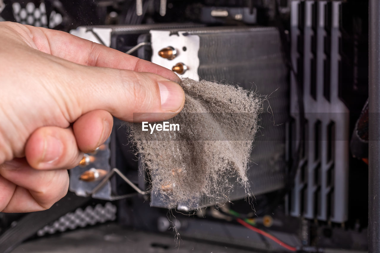 Bare caucasian hand holding dust clog in front of opened pc case during maintenance