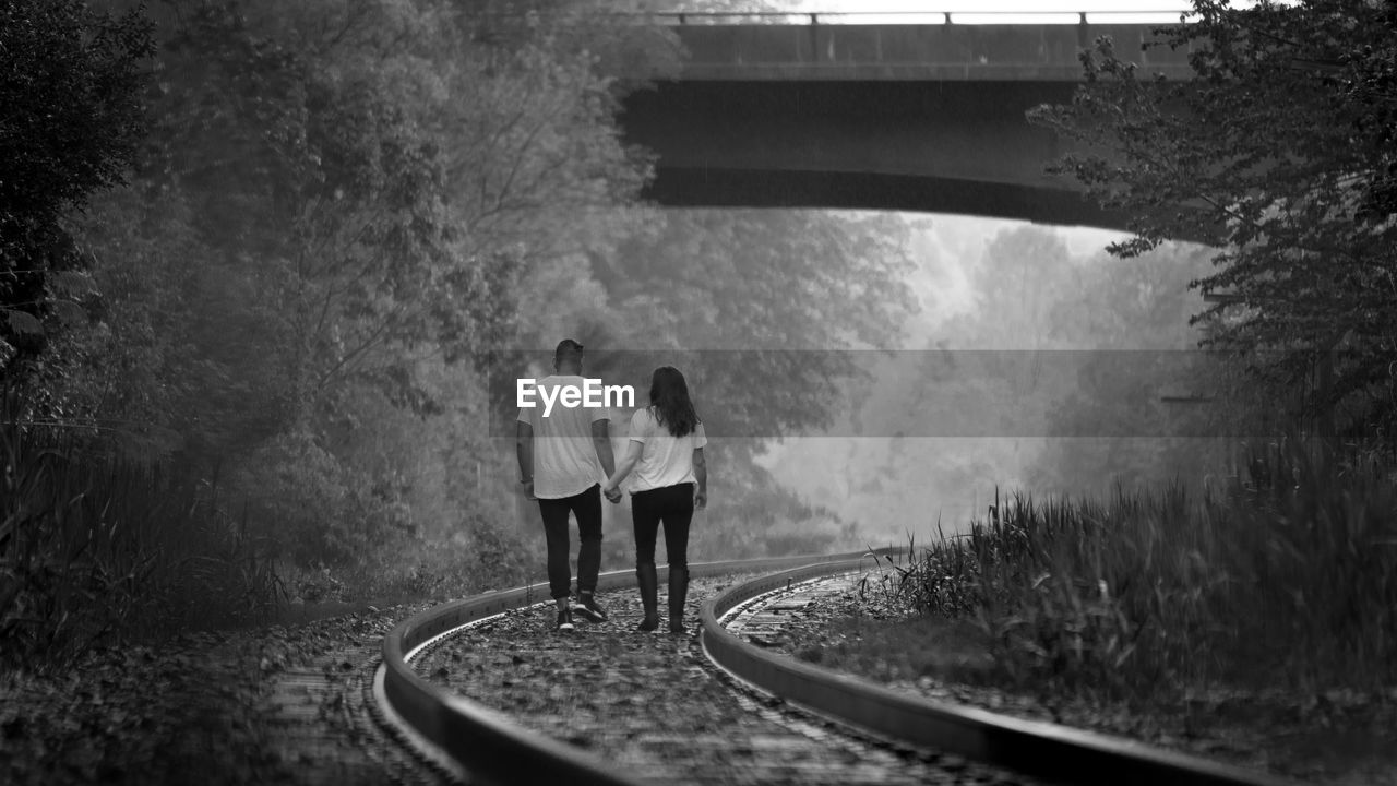 Rear view of friends walking on railroad tracks during foggy weather