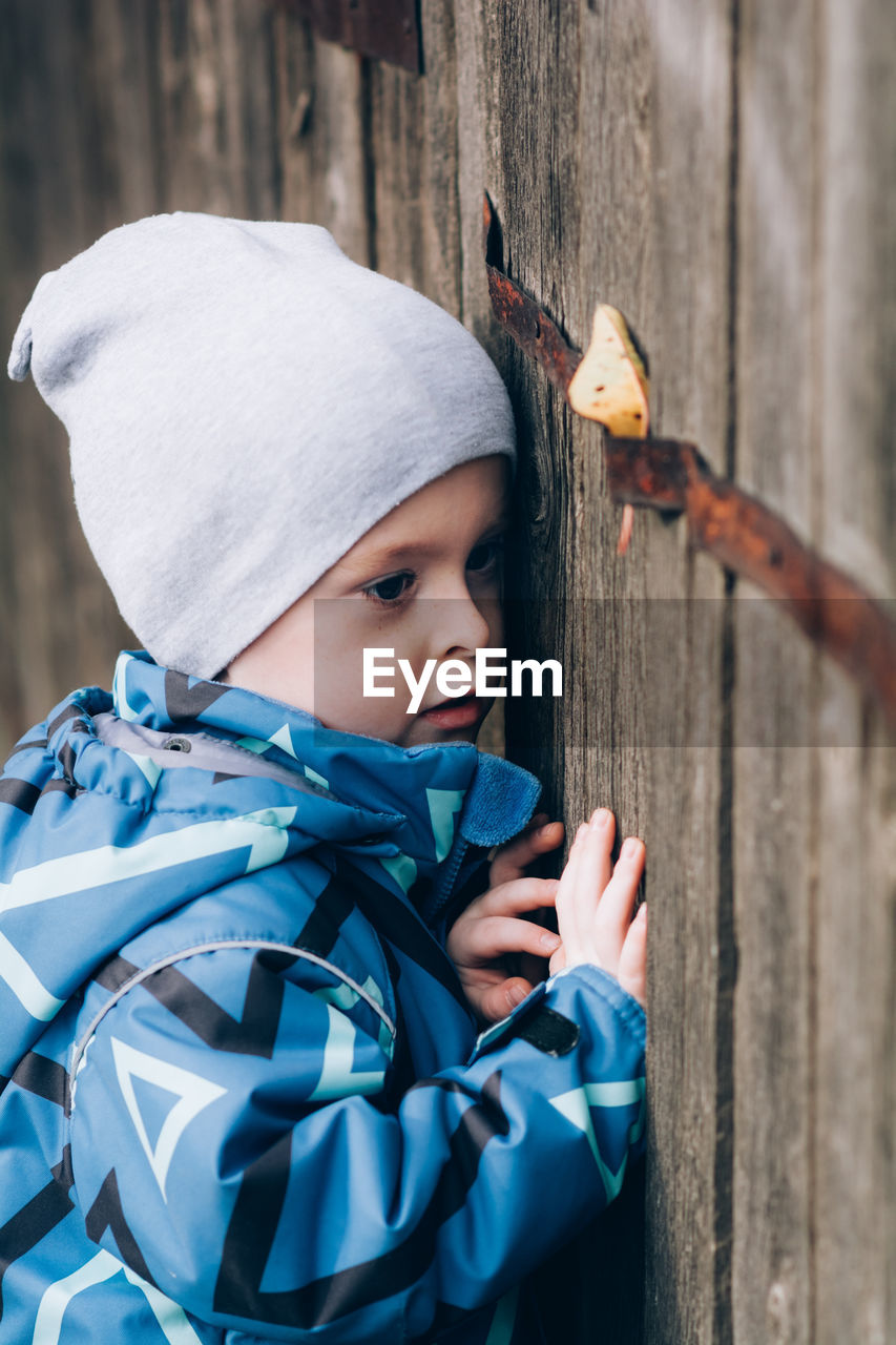 A child peeks through a wooden fence. curious, inquisitive boy explores