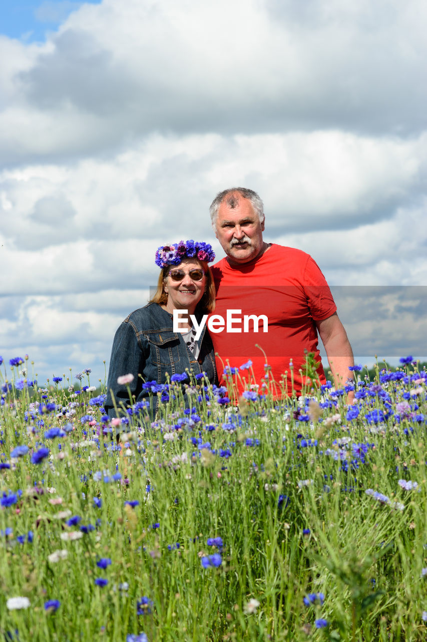 Married couple in the middle of a colorful field of cornflowers enjoying summer, sky full of clouds