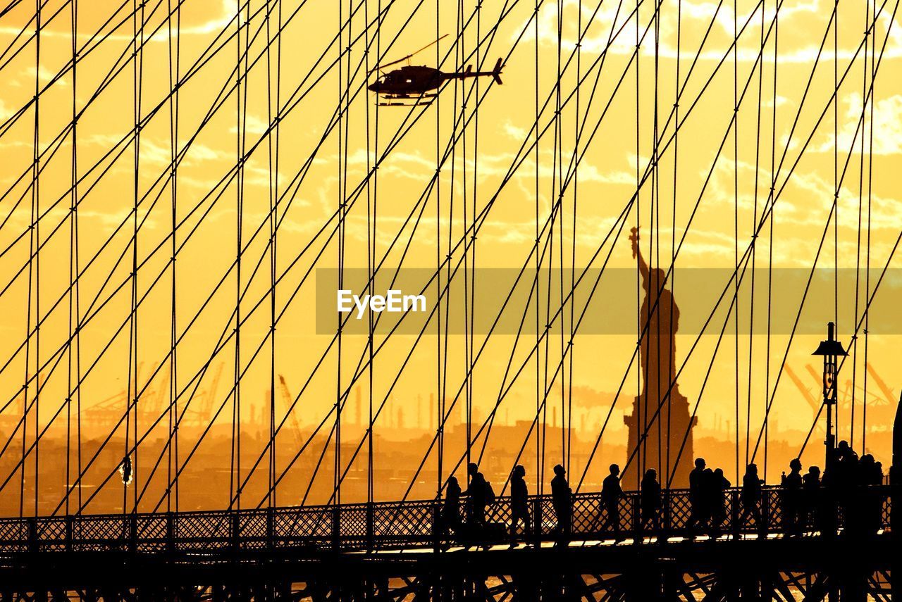 Silhouette of brooklyn bridge against statue of liberty at sunset