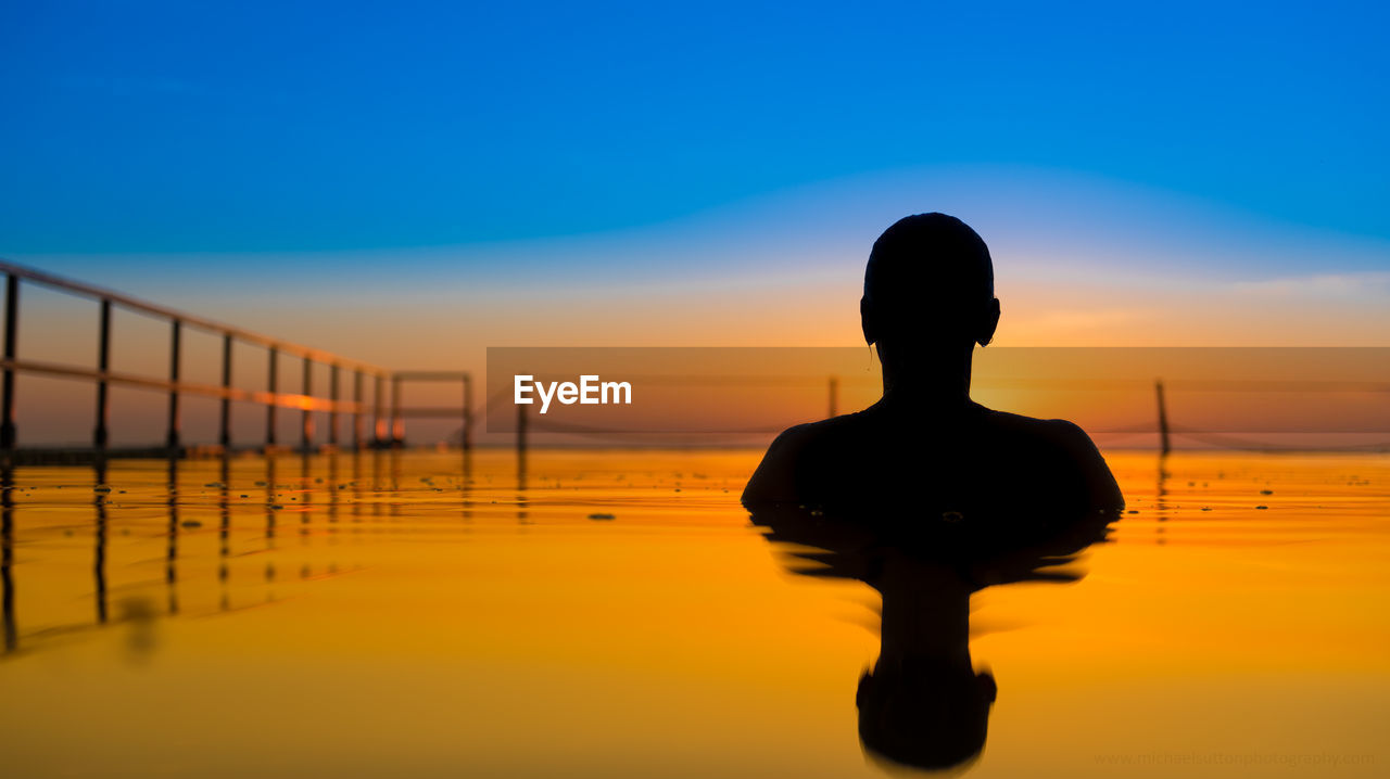 Silhouette person in sea against dramatic sky during sunset