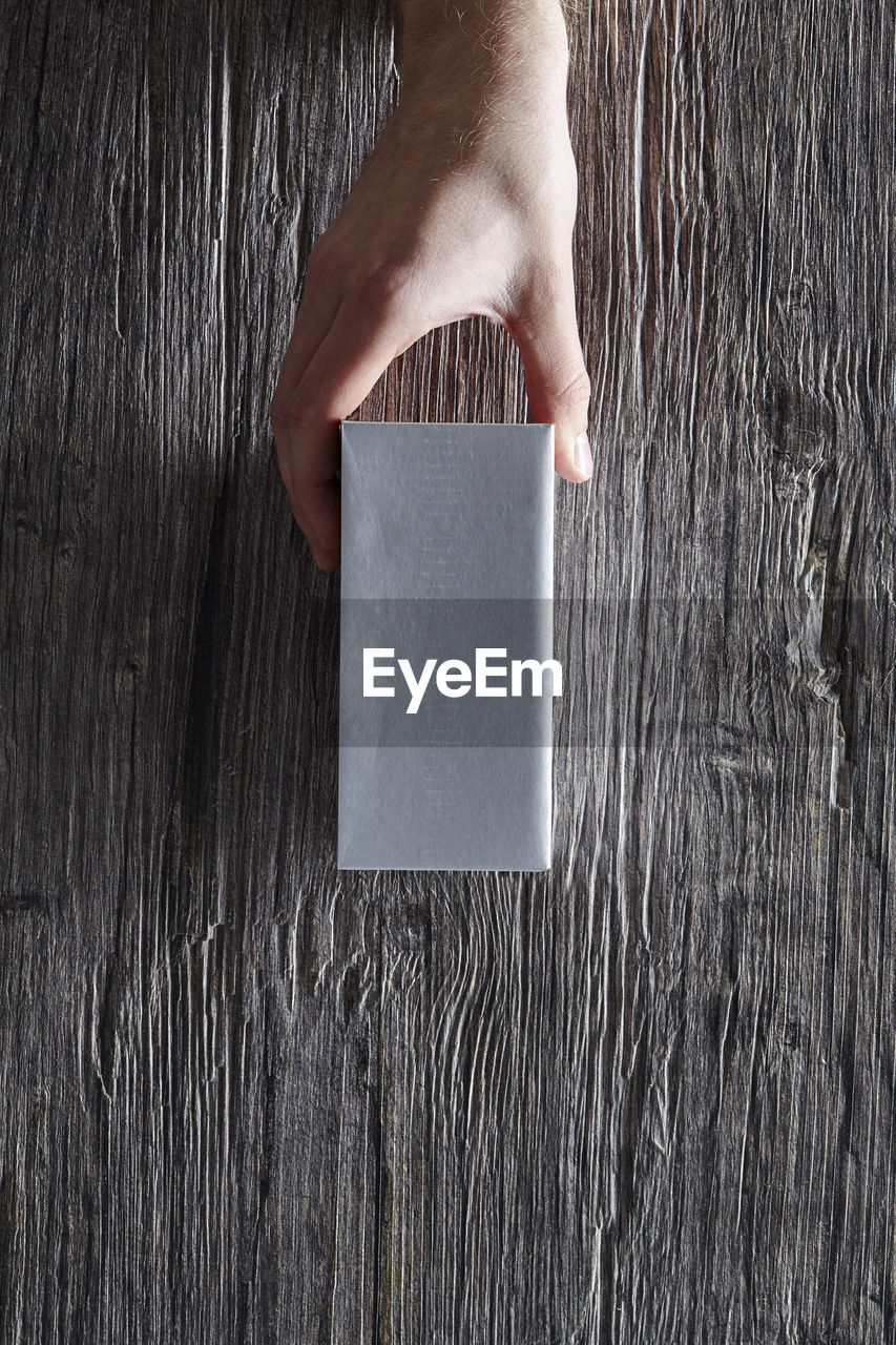 Close-up of hand holding box against wooden wall