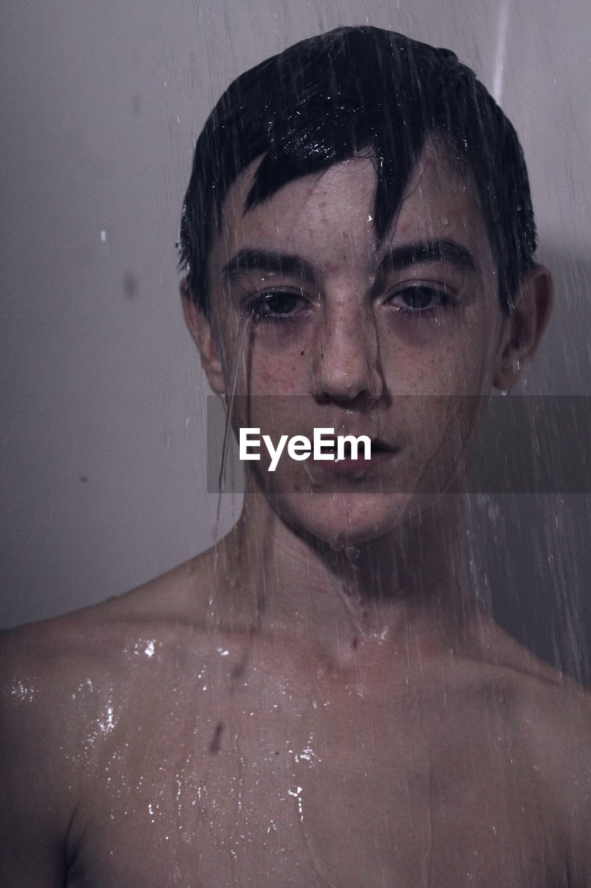 Close-up portrait of teenage boy under shower in bathroom