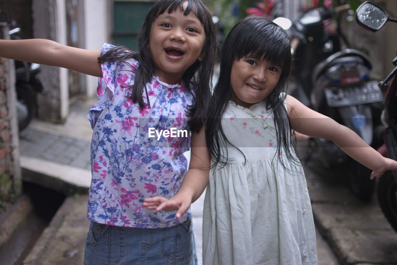 Portrait of happy sisters standing in alley