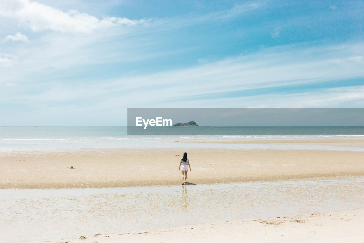 Rear view of woman walking at beach against sky
