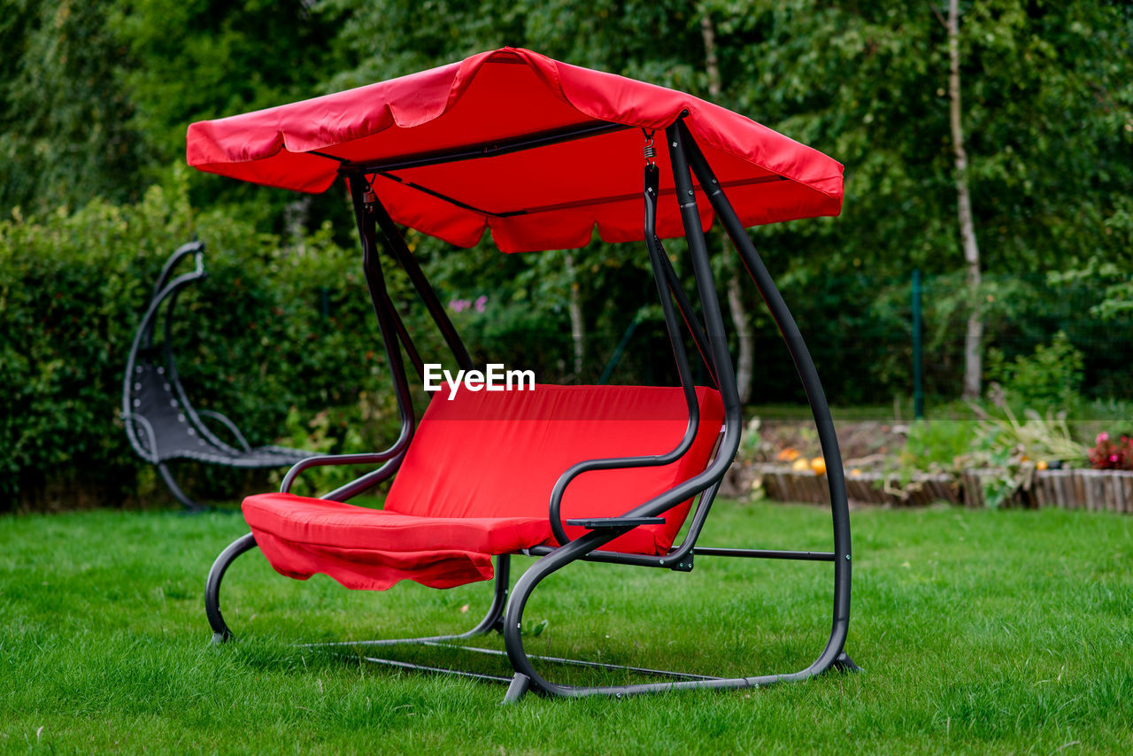 Empty red swing bench on grassy field at yard