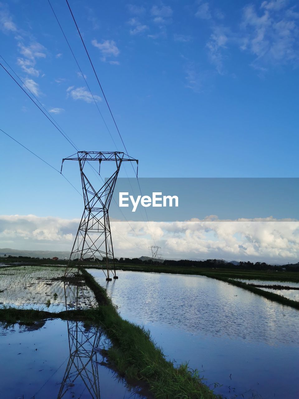 ELECTRICITY PYLONS BY LAKE AGAINST SKY