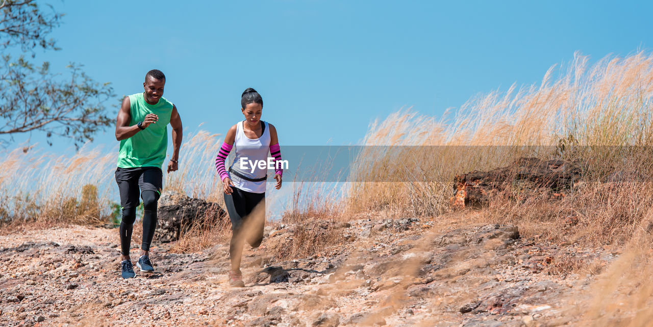 Full length of couple running on land against sky