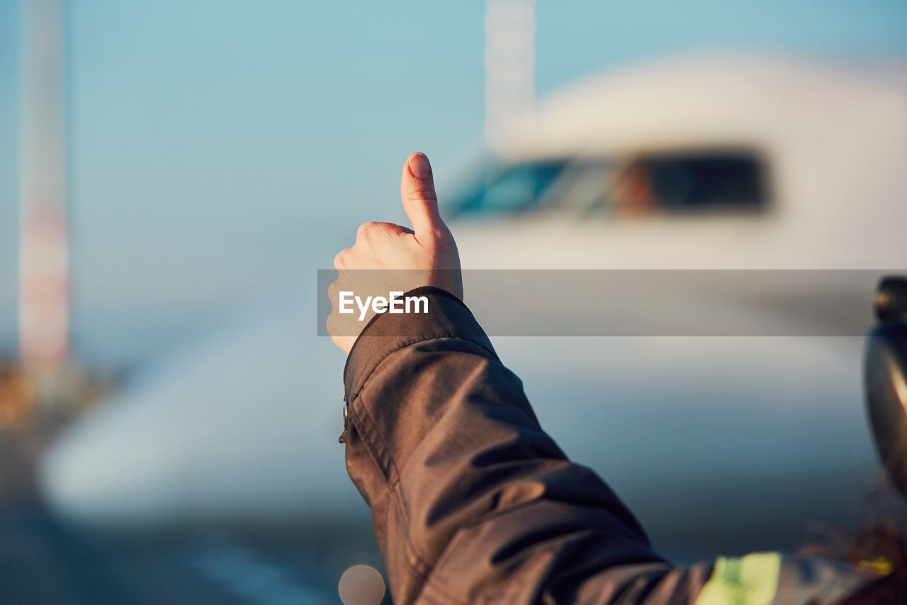 Cropped image of man gesturing against airplane at airport runway