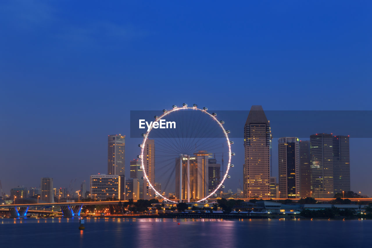 ILLUMINATED FERRIS WHEEL BY RIVER AGAINST SKY