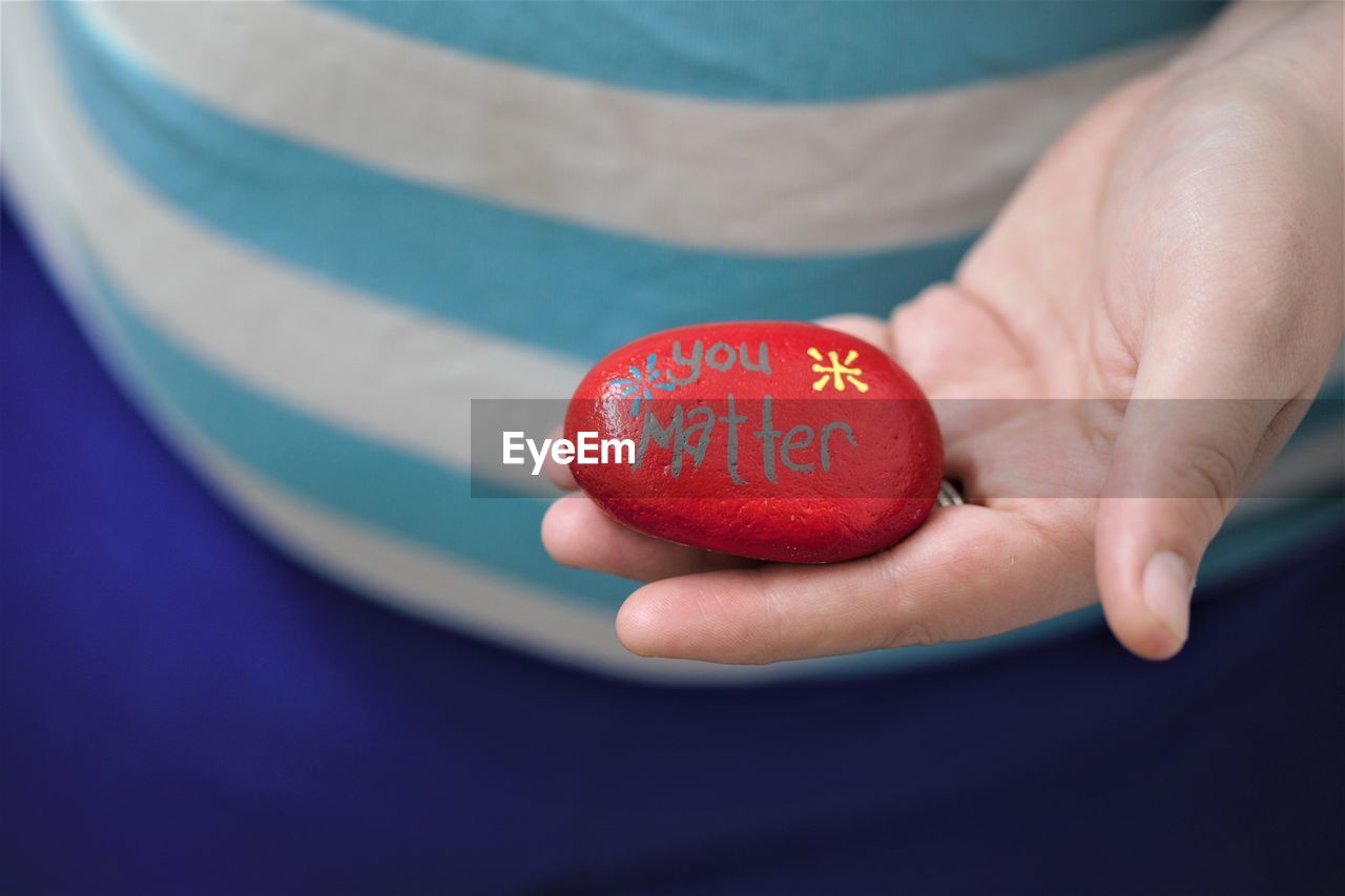 Midsection of woman holding red pebble with text