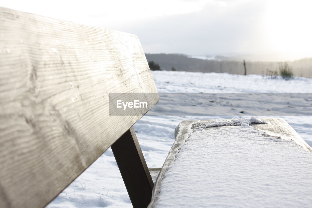 Close-up of wooden bench on snow covered field