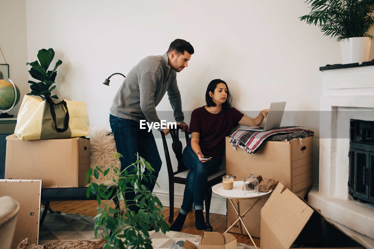 Woman showing laptop to man while moving at new home